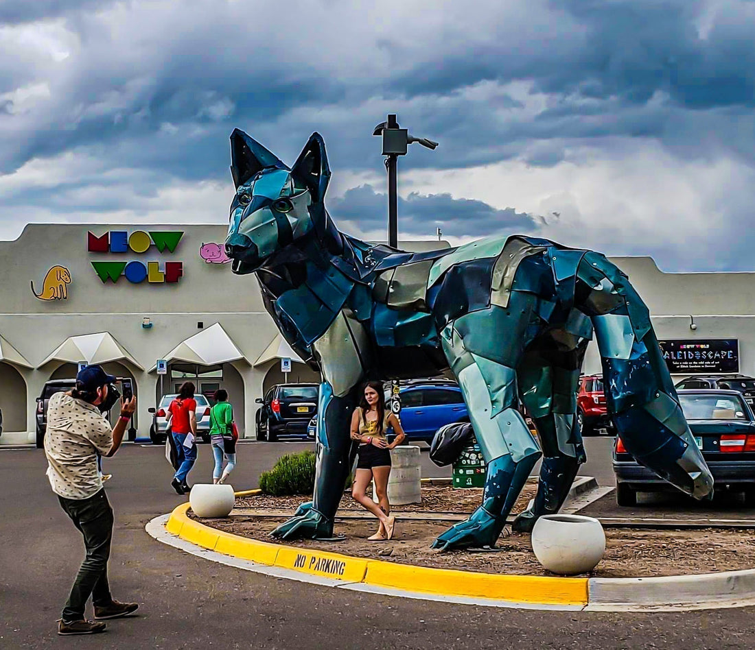 Large blue wolf sculpture outside an art installation with visitors nearby.