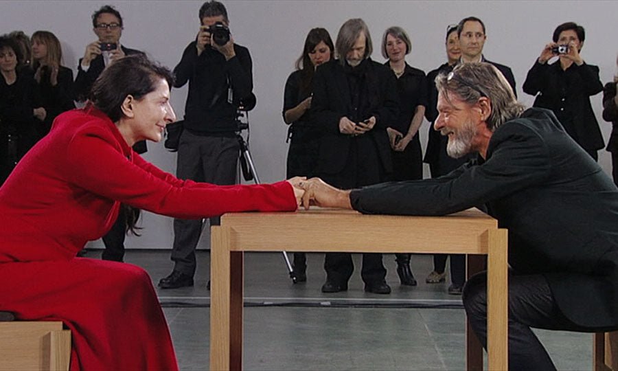 Two people seated across from each other in a museum performance setting.