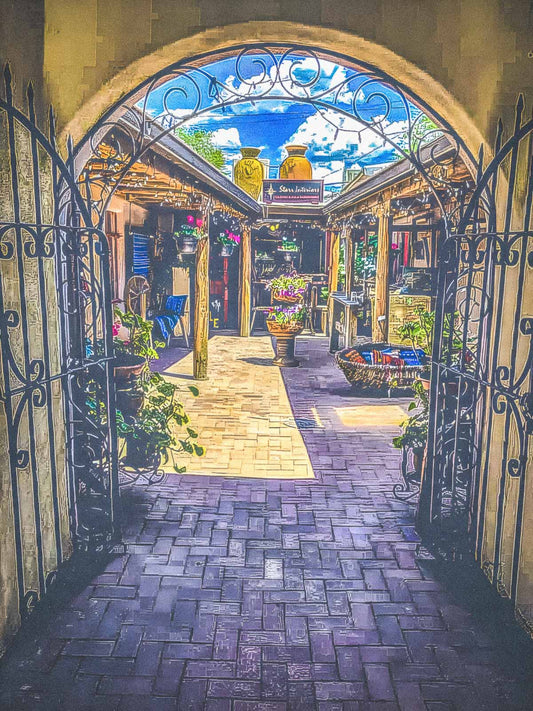 Decorative archway leading to a courtyard in Taos, New Mexico with shops and plants