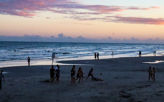 People playing beach basketball at sunset with a colorful sky.