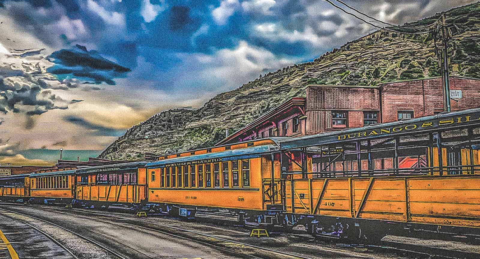 Vintage train on tracks with a mountainous landscape and blue sky.
