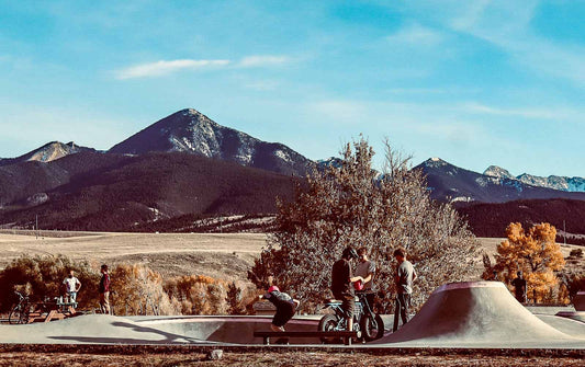 People with skateboards and bicycles in a skate park with mountains in the background