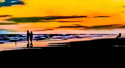 Two people walking on a beach at sunset with colorful sky