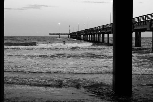 Black and white photo of a pier extending into the ocean with waves crashing against it.