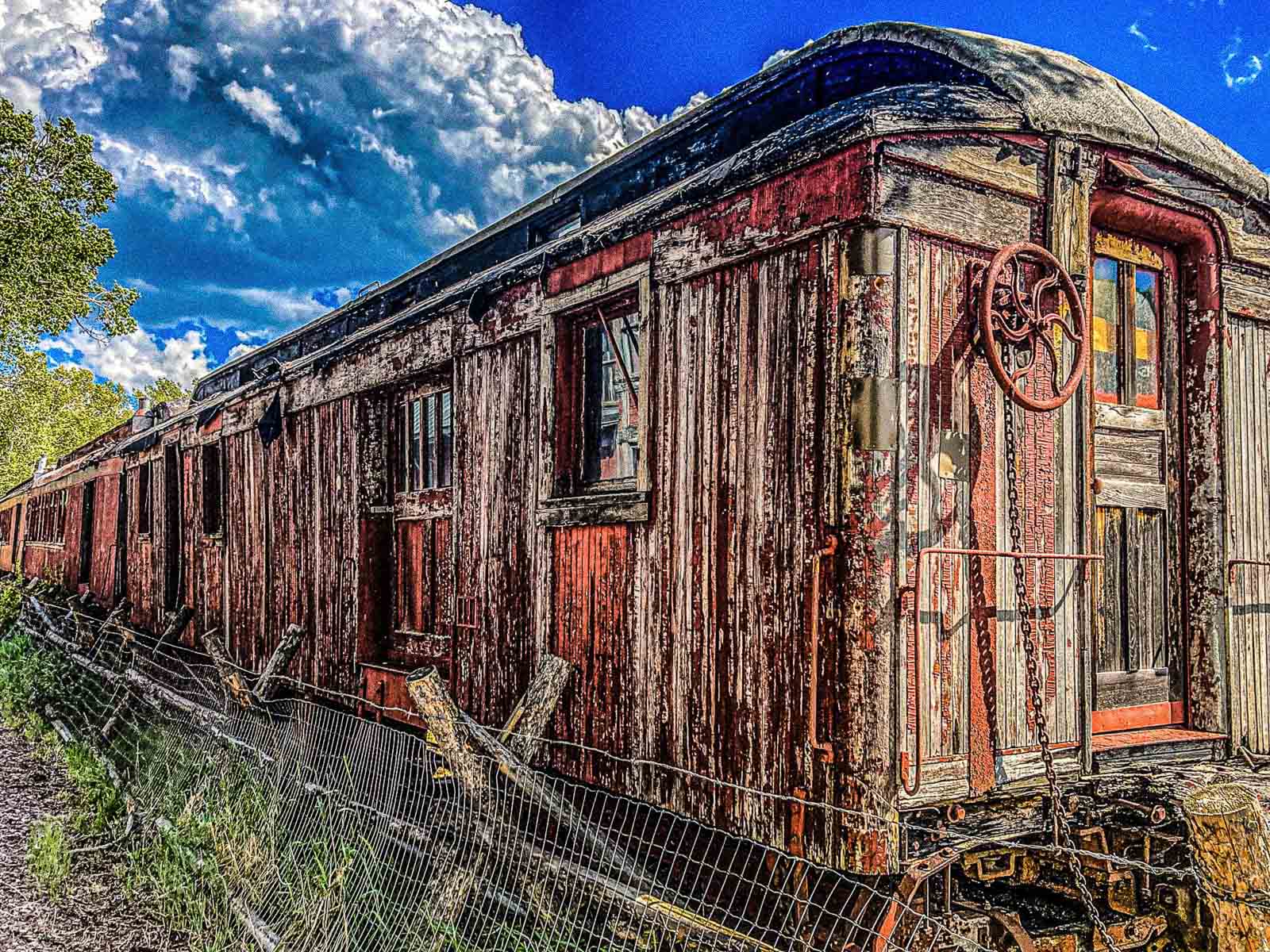 Old wooden train car with rust and peeling paint against a blue sky.