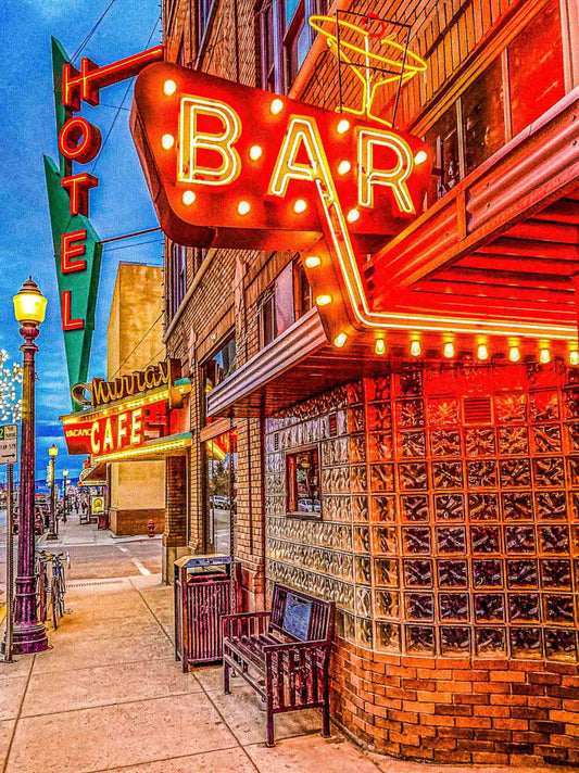 Neon signs for a bar and hotel on a city street at night.